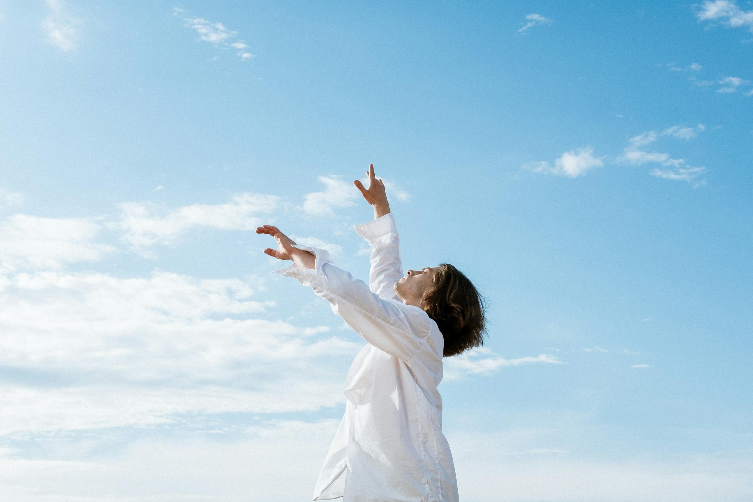 Man in white shirt dancing gracefully outdoors under a clear blue sky.