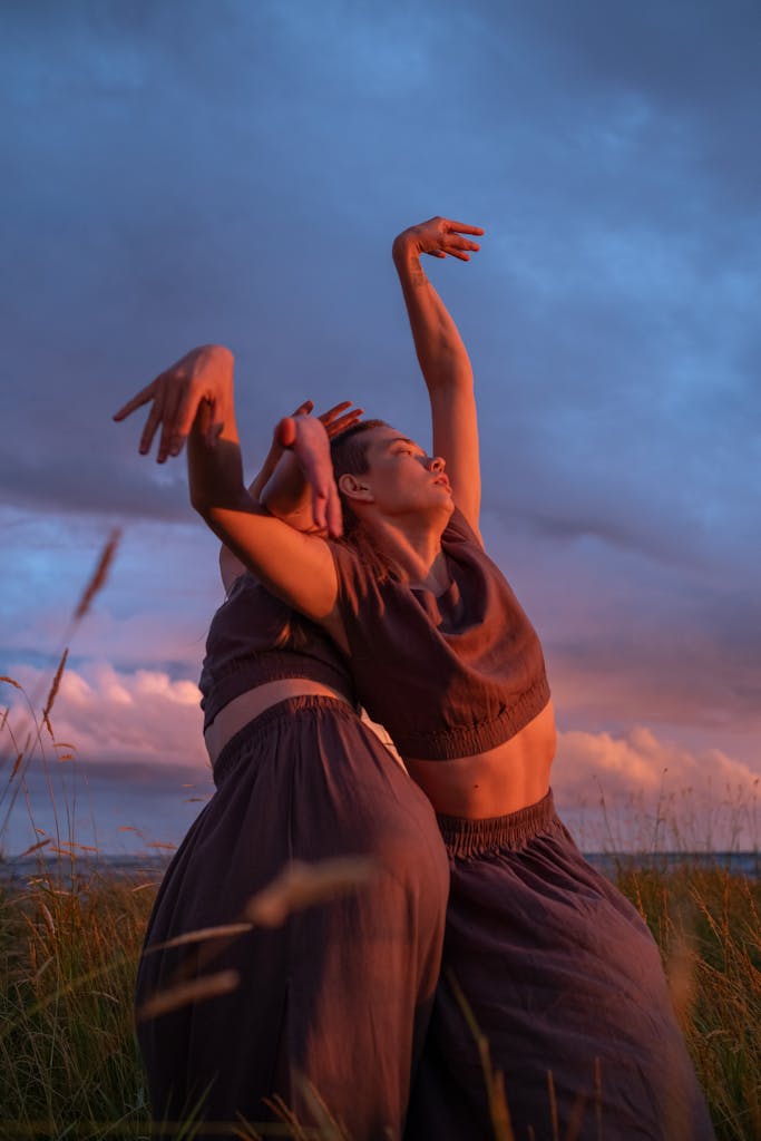 Two women gracefully dancing in a grassy field at sunset.